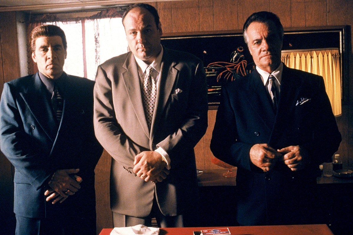 Three older mobster men in suits, somber expressions, crossed arms, video still from The Sopranos.