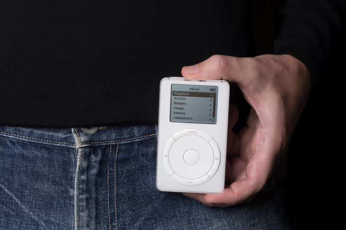 A close cropped image of a hand holding a chunky electronic device with a circular navigational button and digital screen.