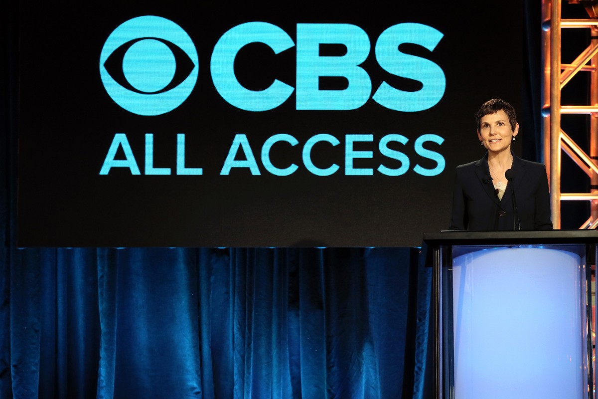 A woman stands at a podium in front of a large screen that reads CBS All Access